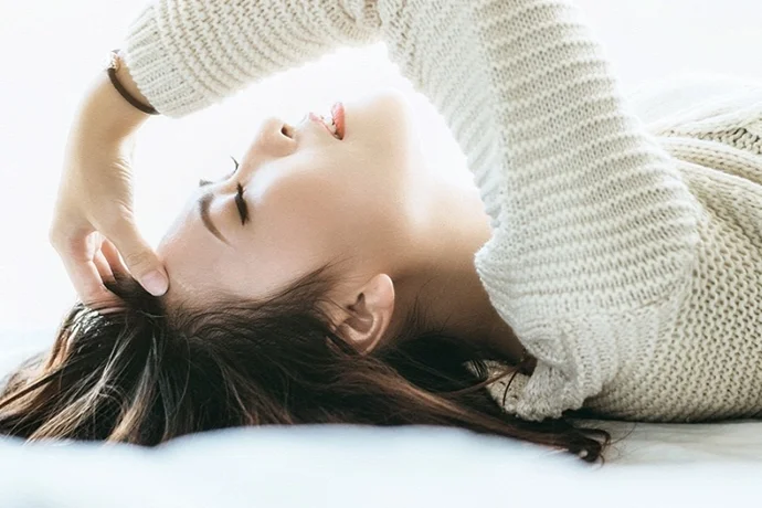 頭をおさえてベッドに横になる女性