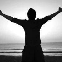 海に向かって両手を広げる男性の後ろ姿