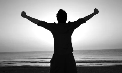 海に向かって両手を広げる男性の後ろ姿