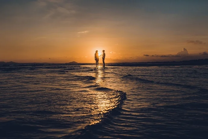 水辺で手を繋ぐ男女のシルエット