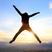 山の頂上で朝日を浴びながら両手を広げジャンプする男性のシルエット写真